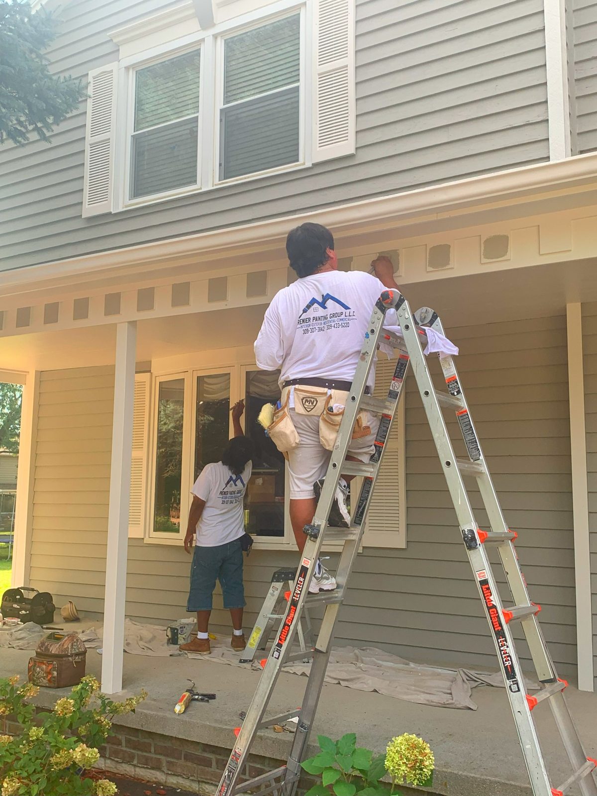 Premier Painting Group crew painting the exterior trim of a two-story home from ladders